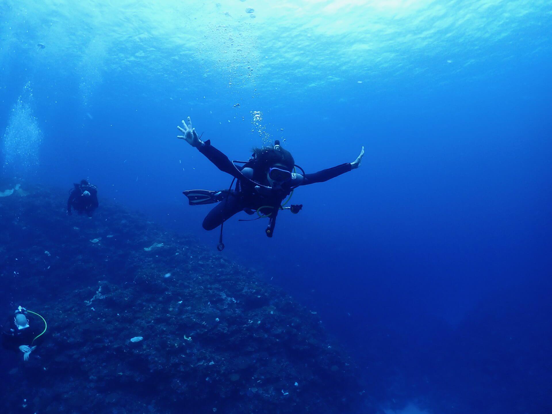 A diver in Okinawa, with arms spread wide, enjoying the underwater environment.